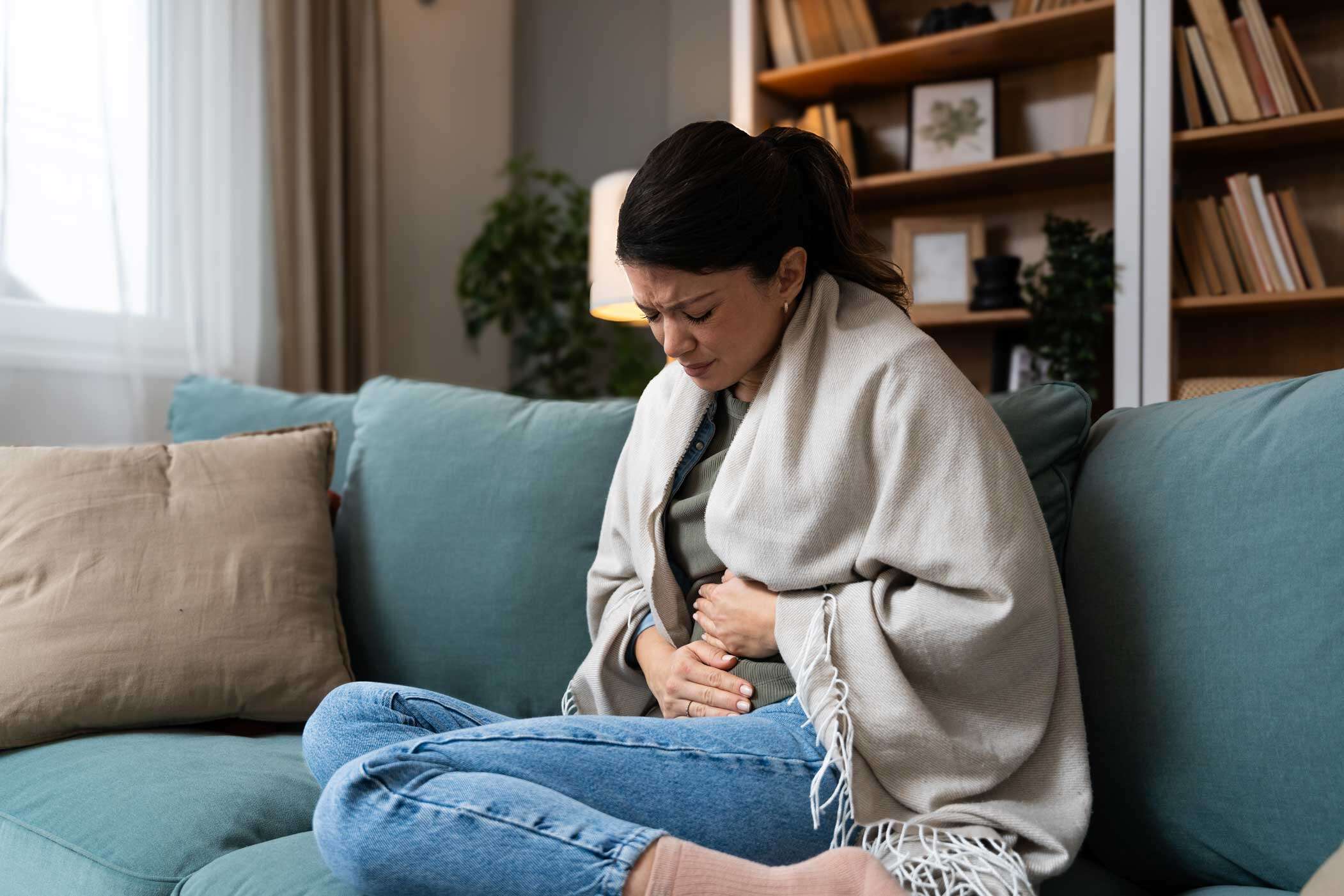 Frau hält ein hustendes Kind im Arm und hält ein Fieberthermometer in der Hand.